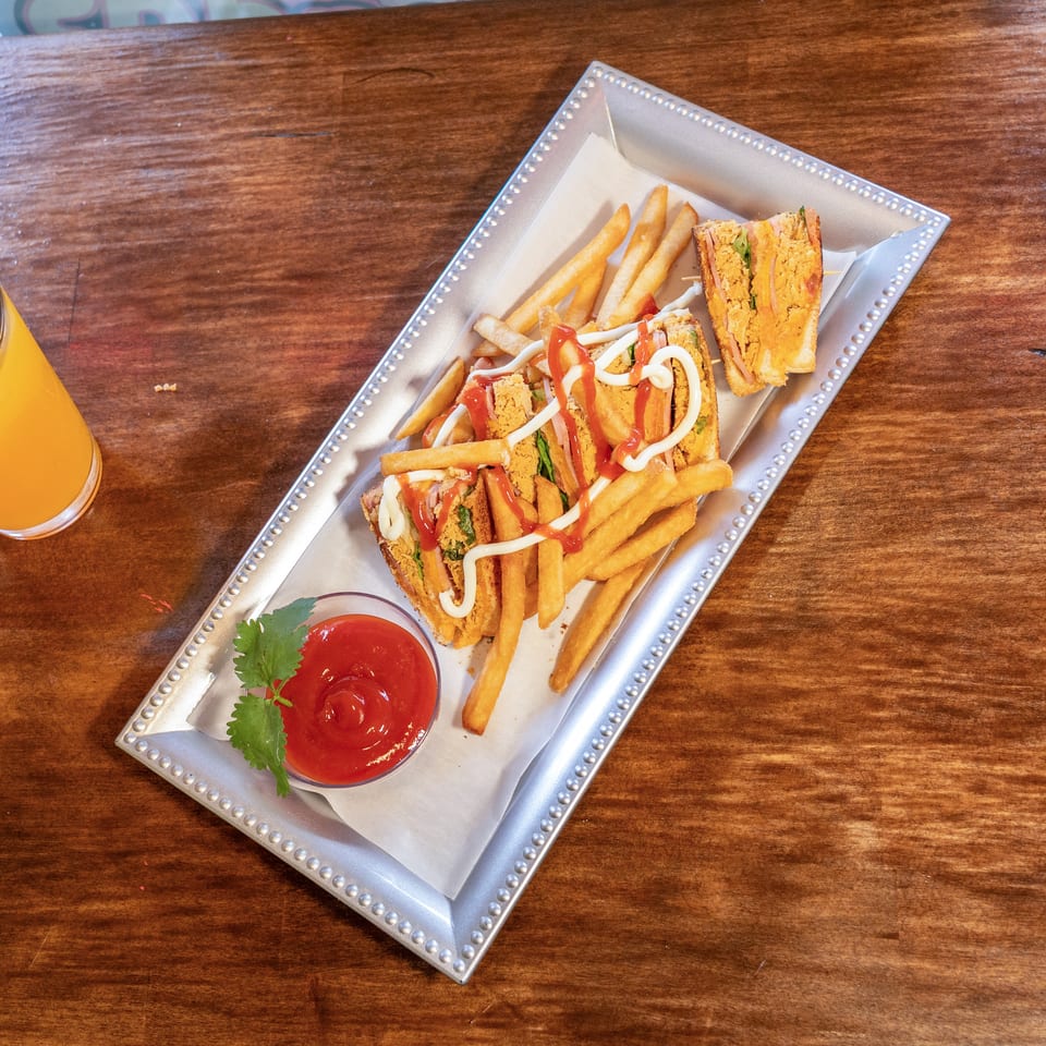 A silver tray holds a club sandwich with fries, ketchup, and mayonnaise, next to a glass of orange juice.