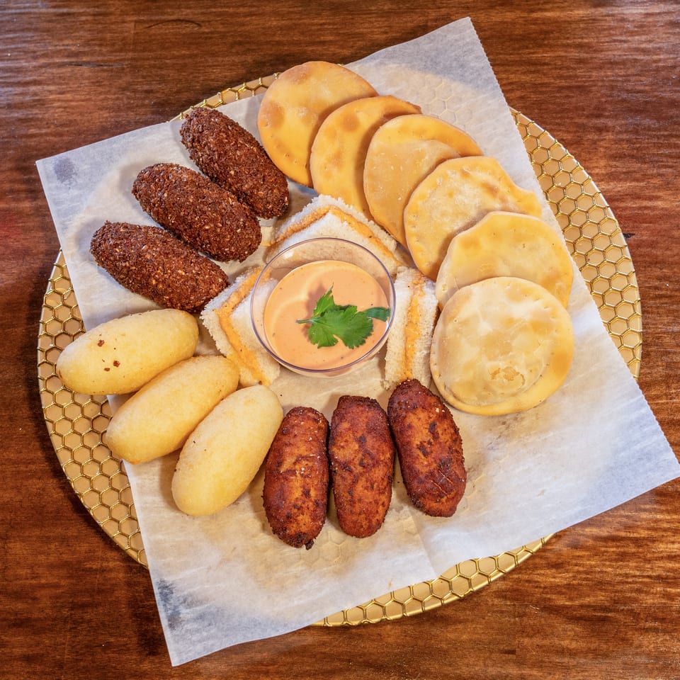Assortment of fried appetizers including empanadas, croquettes, and corn fritters with a dipping sauce.