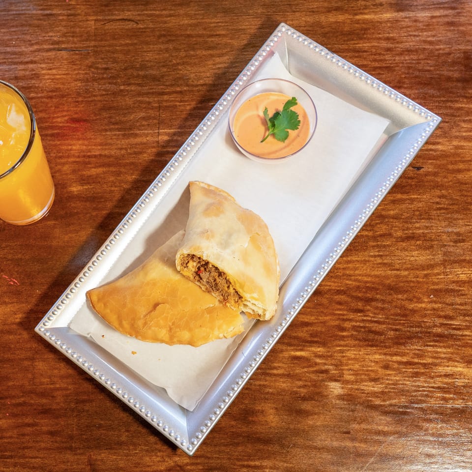 Two empanadas, one cut open to show the filling, with dipping sauce and orange juice.