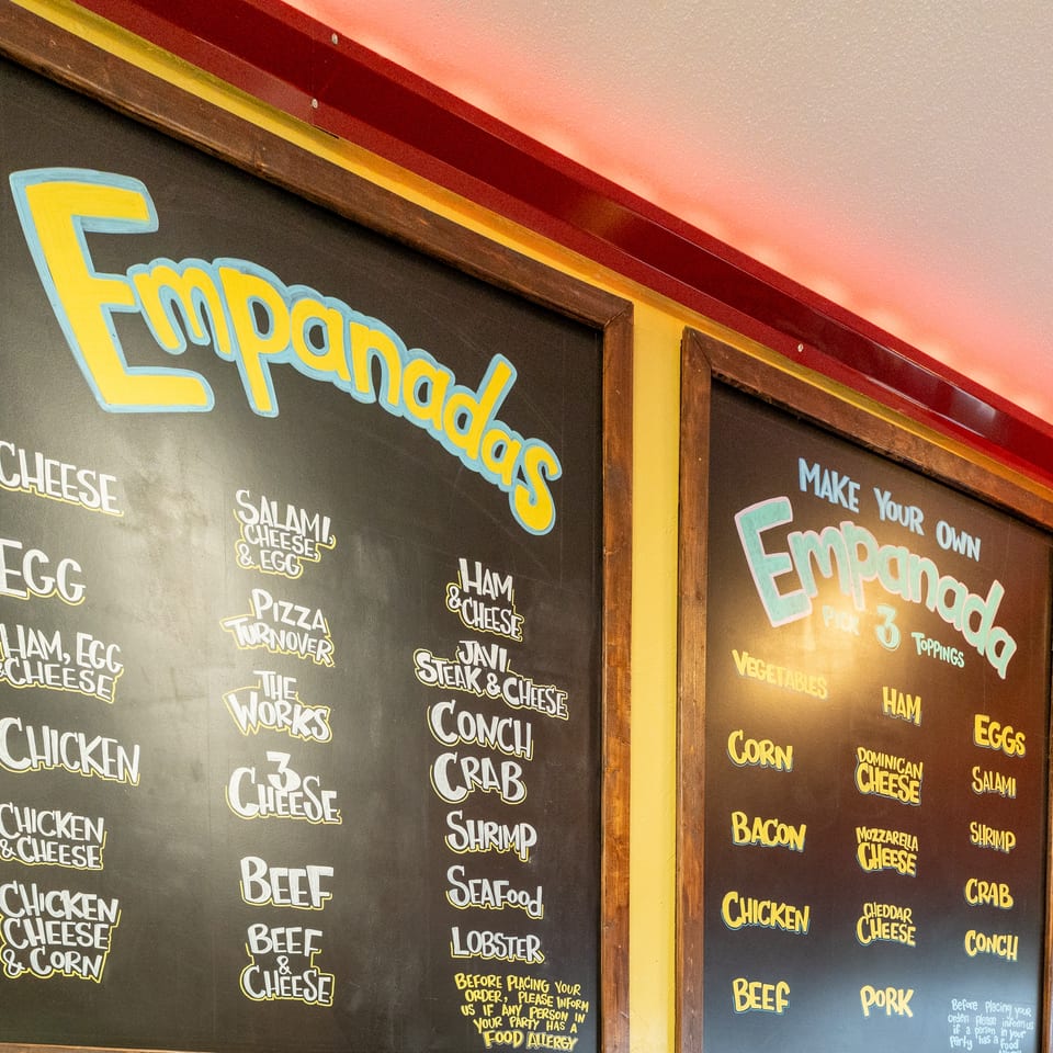 Two chalkboards display a menu of empanada fillings and toppings, including cheese, chicken, and seafood.