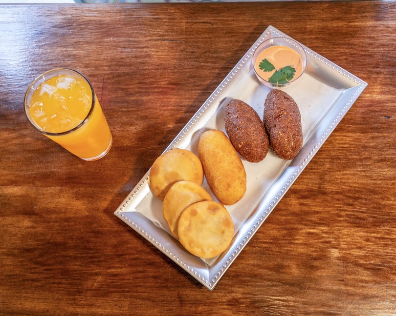Assortment of fried pastries, including empanadas and kibbeh, with a dipping sauce and orange juice.