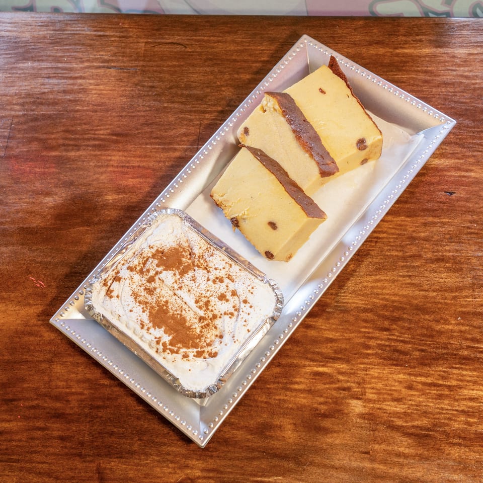 Three slices of bread pudding with raisins and a container of tiramisu on a silver tray.