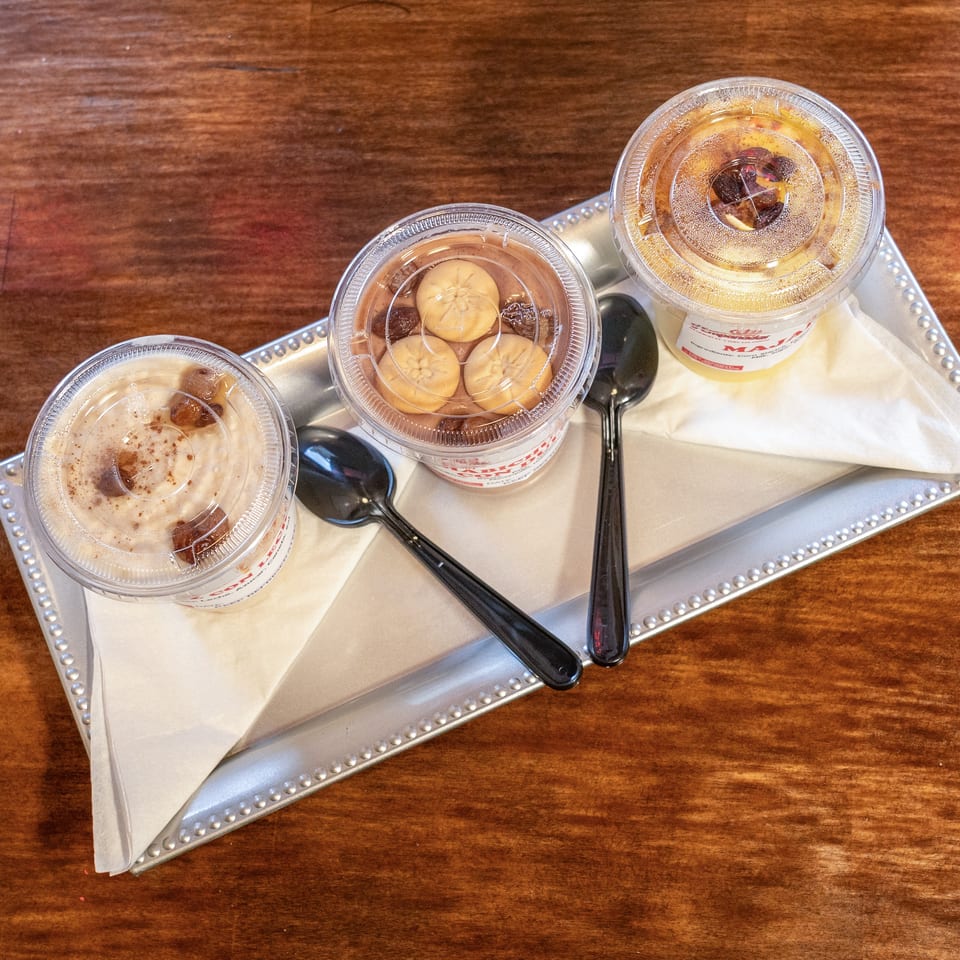 Three plastic cups of desserts with spoons on a silver tray, on a wooden table.