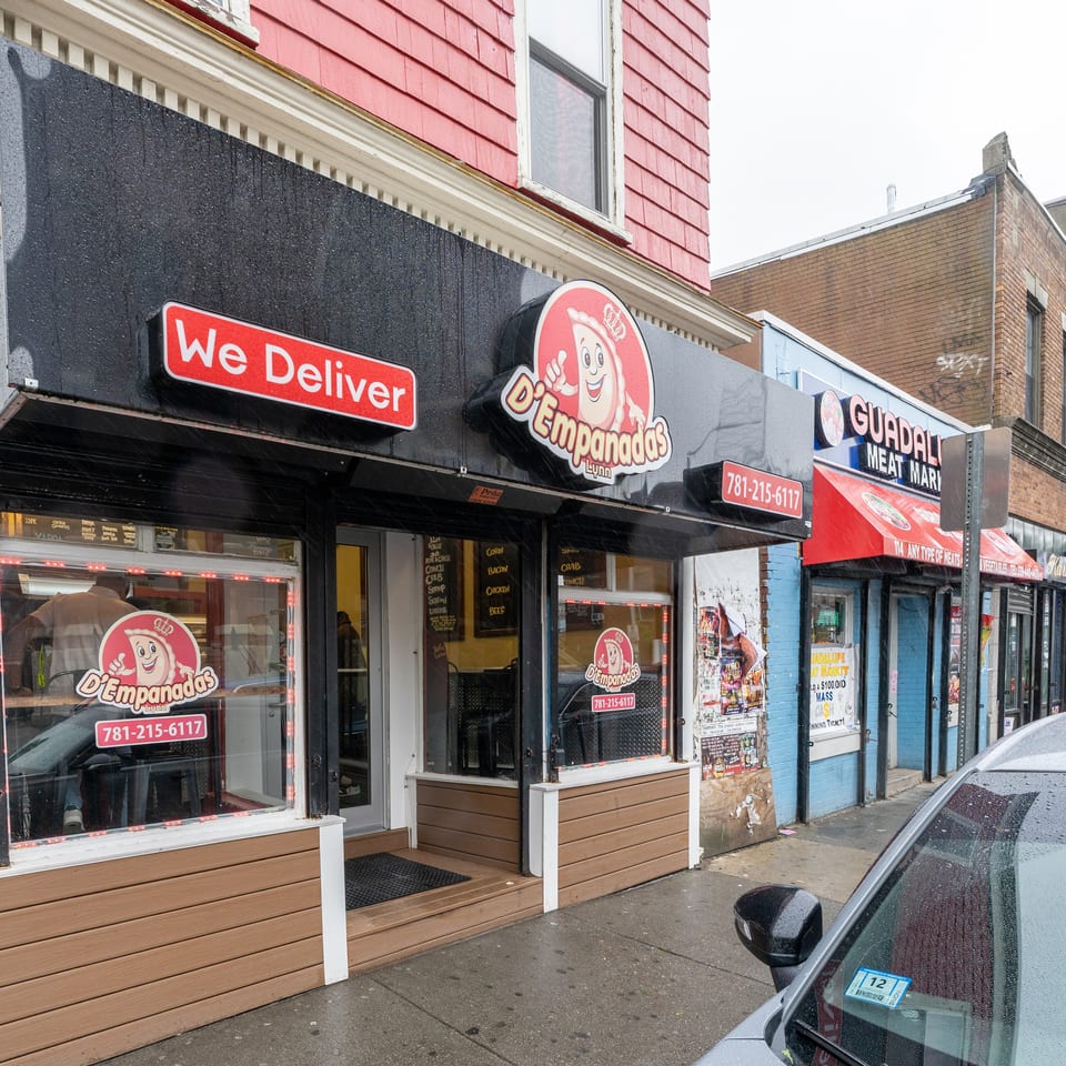 Exterior of D'Empanadas restaurant with a "We Deliver" sign and a car parked nearby.