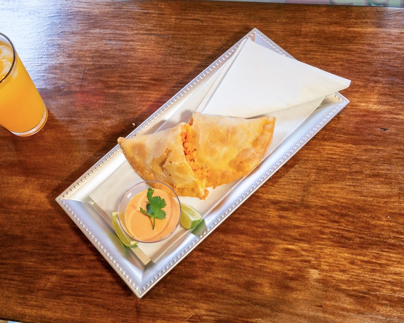Golden-brown empanada, split open to show a vibrant orange filling, served with sauce and lime.